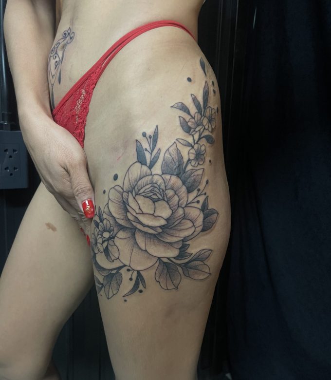 Black and grey floral thigh tattoo with fine-line details by Mr.X at Dragonking Tattoo Pattaya.