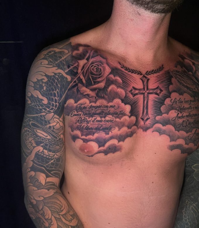 Black and grey religious chest tattoo with cross, prayer script and rose connected to sleeve tattoo in Pattaya