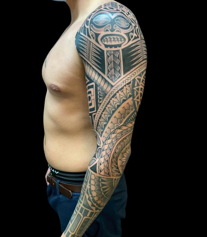 Polynesian full sleeve tattoo with symbolic mask and geometric patterns at Dragon King Tattoo Pattaya