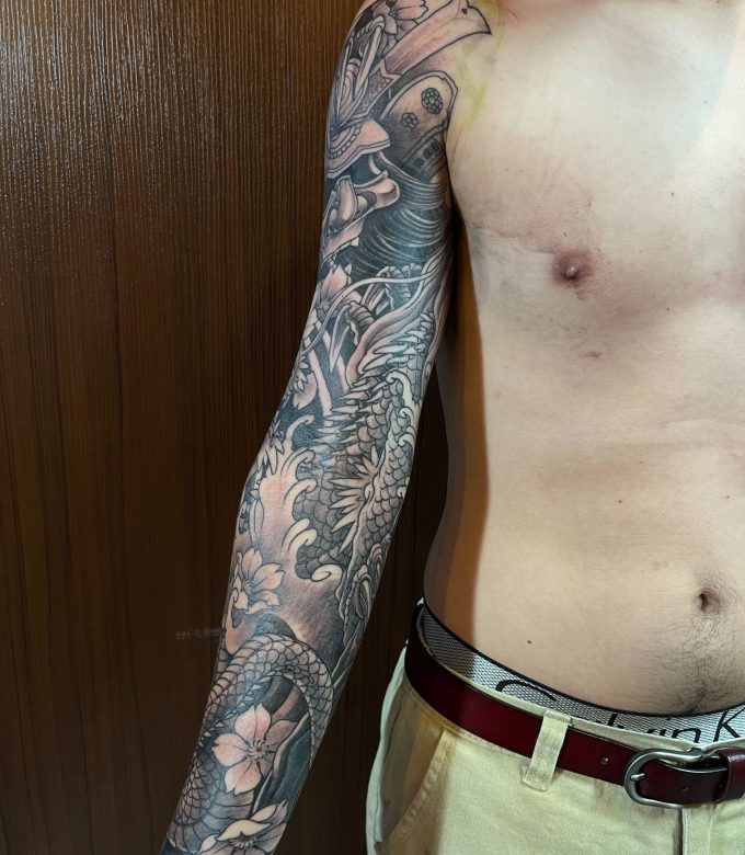 Black and grey Japanese full sleeve tattoo in progress, freehand dragon and traditional elements designed to fit the arm flow by Dragonking Tattoo Pattaya