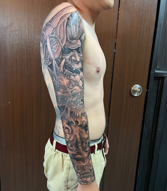 Black and grey Japanese full sleeve tattoo side view, freehand dragon and traditional motifs flowing from shoulder to forearm by Dragonking Tattoo Pattaya