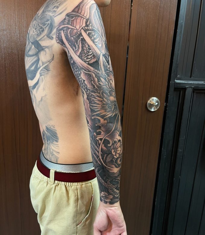 Back side view of black and grey Japanese full sleeve tattoo, freehand dragon and traditional elements wrapping naturally around the arm by Dragonking Tattoo Pattaya