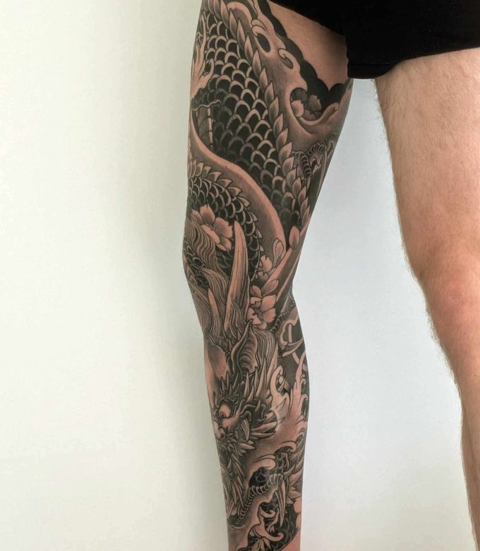 Japanese black and grey leg sleeve tattoo with dragon and wave elements, custom design by Dragonking Tattoo Pattaya