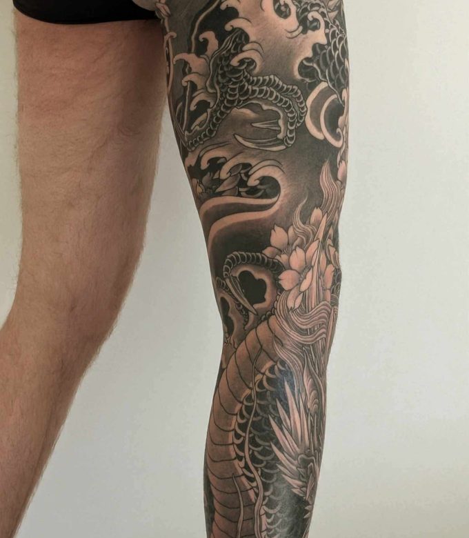 Japanese dragon leg sleeve tattoo with floral elements in black and grey by Dragonking Tattoo Pattaya